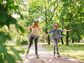 Eine Frau und ein Kind rollerbladen durch einen grünen Park.